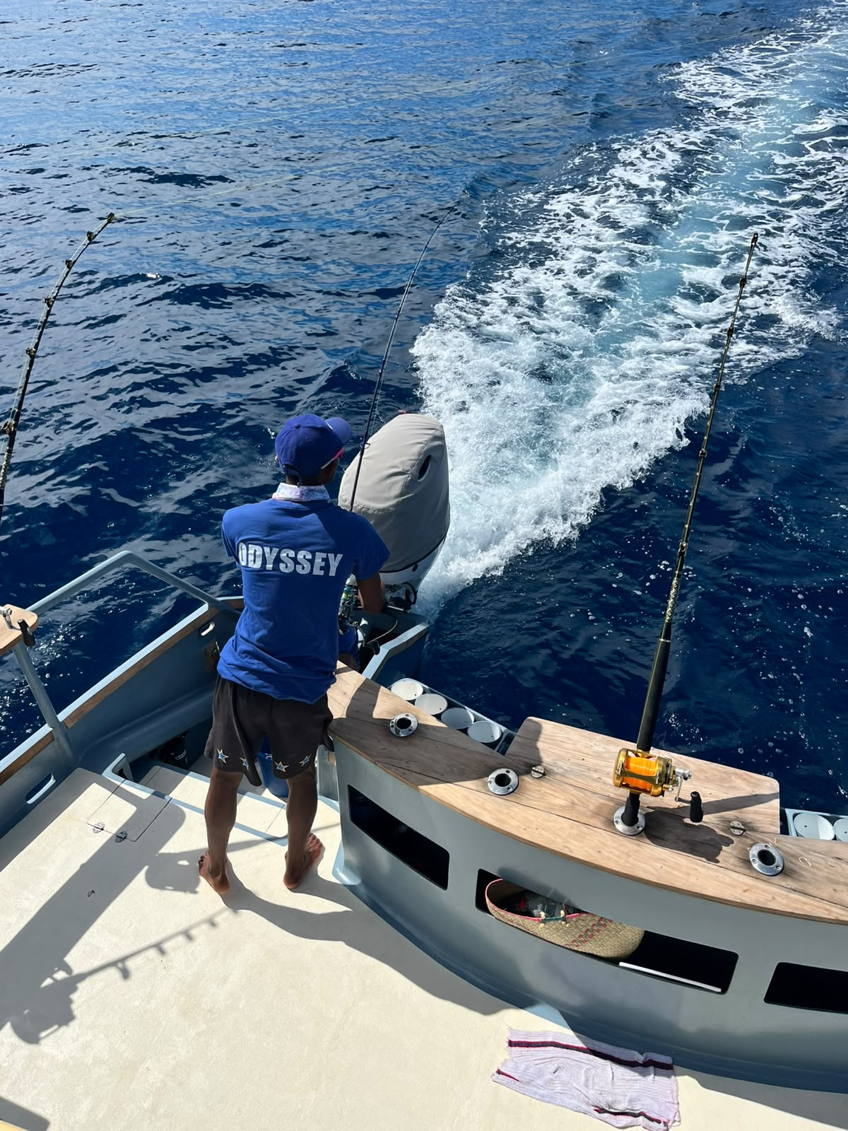 An AAM crew member in a blue Odyssey shirt tending trolling rods from the stern while running across deep blue water
